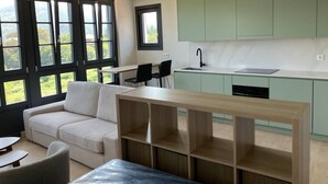 Une cuisine moderne avec des meubles de couleur vert clair, un four encastré et un coin repas comprenant un canapé et des chaises blancs.
