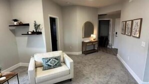 A spacious living room with a white sofa, a small table, and a bookshelf.