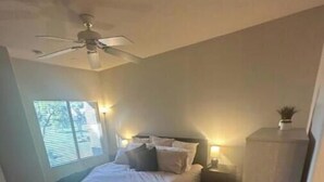 A bedroom with a bed, a ceiling fan, a nightstand, and a small cabinet.