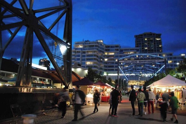 Un paseo marítimo con gente caminando, una gran estructura metálica y el edificio 'WALLACE SHIPYARDS' al fondo.