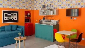 A compact living space with a kitchenette, a sofa, a dining table with colorful chairs, and a TV mounted on the wall. - A.R.T. Loft Trastevere (Roma)