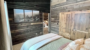 A bedroom with a bed, wooden walls, a large window, and a wardrobe.