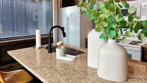 A kitchen with granite countertops, a black faucet, a white vase with green plants, and a white candle holder.