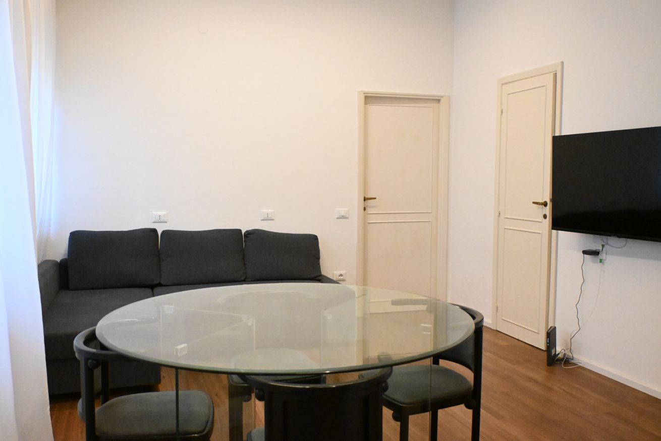 A room with a glass-top table, a sofa, and a TV mounted on the wall.