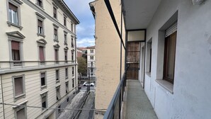 En smal korridor med balkon, tilstødende bygninger og udsigt til gaden.