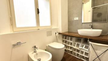 A bathroom with a toilet, bidet, sink, mirror, and storage baskets.
