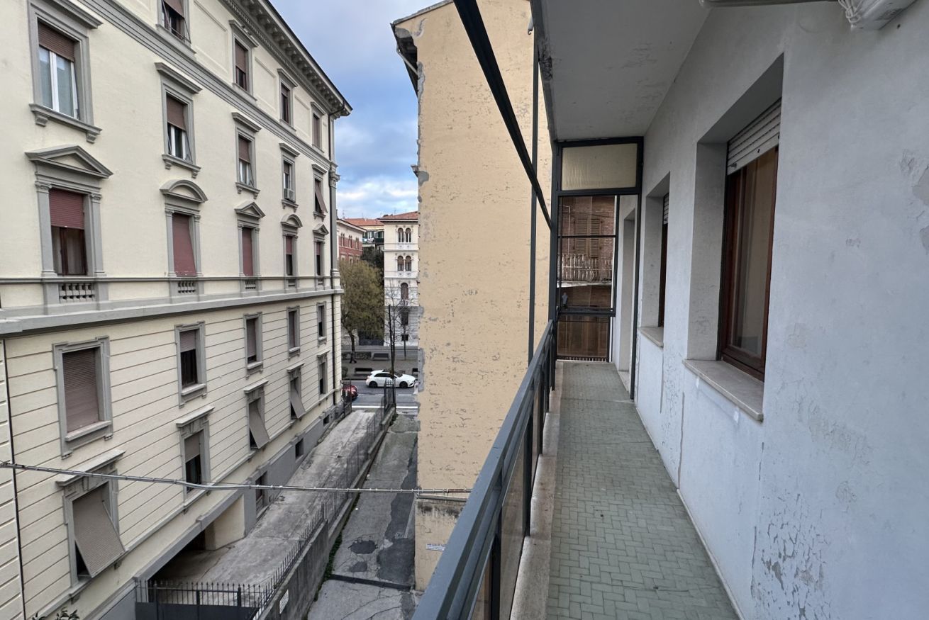 Een smalle gang met een balkon, omliggende gebouwen en uitzicht op de straat.