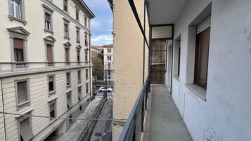 Een smalle gang met een balkon, omliggende gebouwen en uitzicht op de straat.