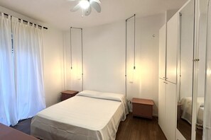 Une chambre à coucher comprenant un lit, des tables de chevet, une armoire et un ventilateur de plafond.