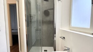 Une salle de bain moderne avec une douche à parois de verre, un lavabo blanc et une fenêtre au-dessus du lavabo.