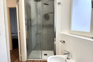 Une salle de bain moderne avec une douche à parois de verre, un lavabo blanc et une fenêtre au-dessus du lavabo.