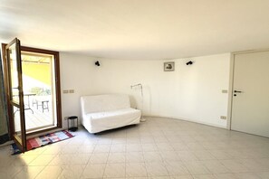 Une pièce avec un canapé blanc, une porte, une petite table et une fenêtre.