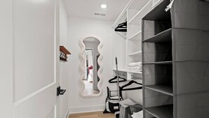 A hallway with a mirror, a coat rack, and a shelving unit with folded clothes.