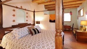 Una cama con dosel con un edredón estampado, techo de madera y un pequeño escritorio con lámpara.