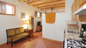 Una habitación acogedora con sofá, lámpara, televisor y una zona de cocina con estufa, además de vigas de madera en el techo.
