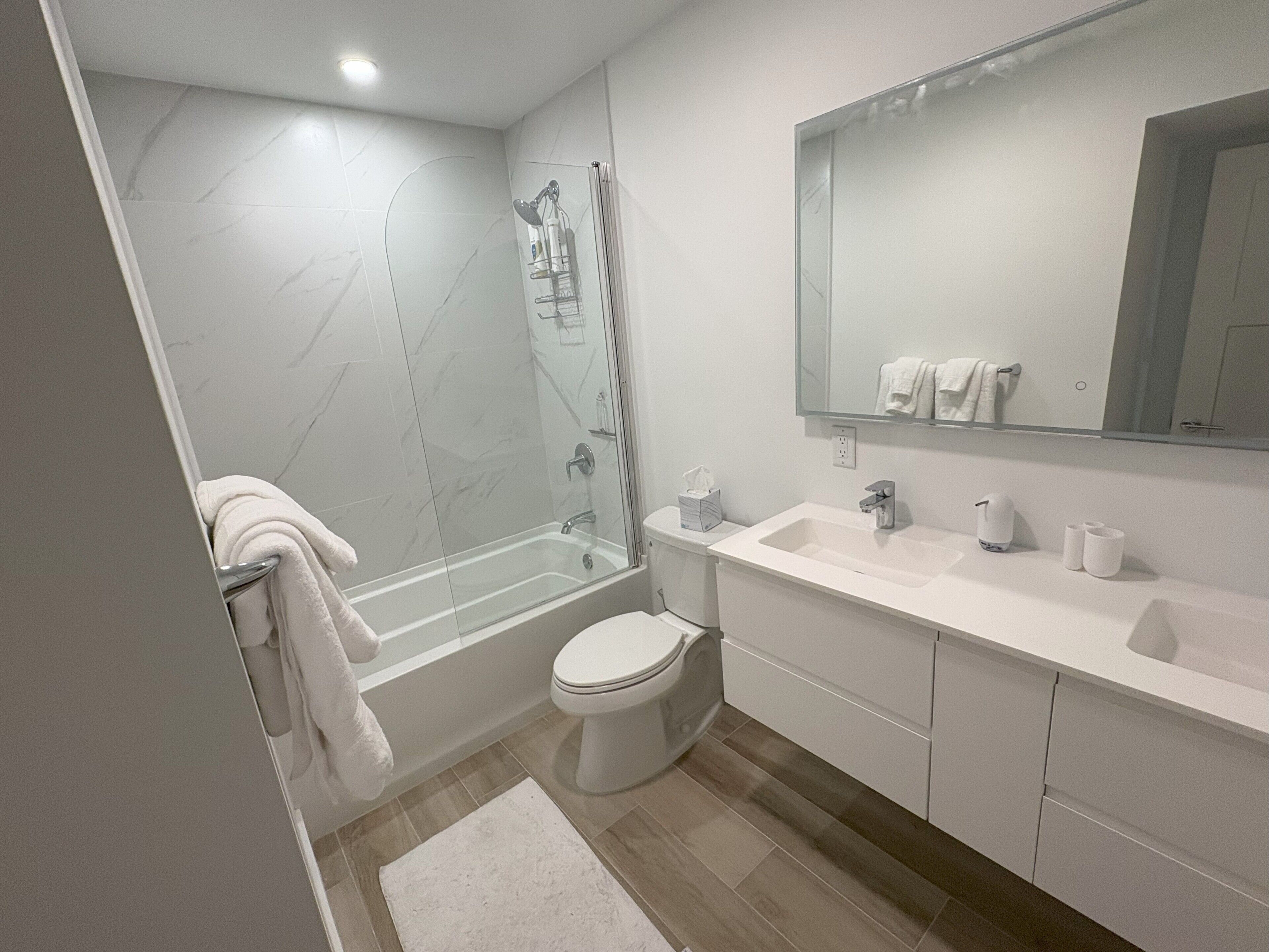 A modern bathroom with a glass-enclosed shower, a white toilet, and a vanity with a mirror.