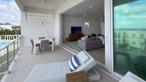 A modern living room with a sofa, TV, and a balcony with a pool view.