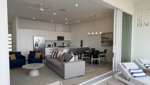 A modern living area with a sofa, chairs, a dining table, and a kitchen in the background.
