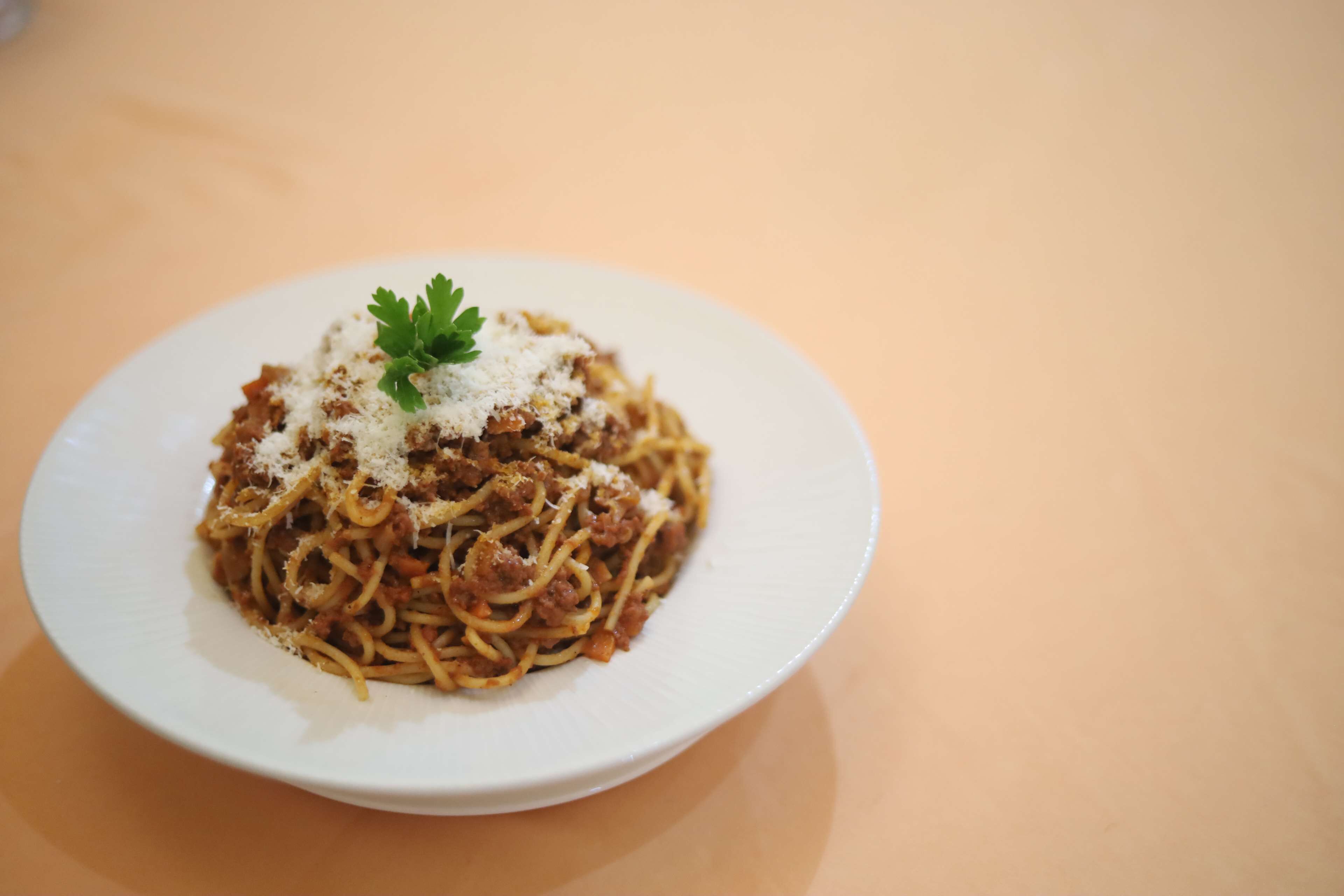 A plate of spaghetti with meat sauce and grated cheese, garnished with parsley, on a white plate.