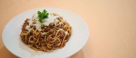 A plate of spaghetti with meat sauce and grated cheese, garnished with parsley, on a white plate.