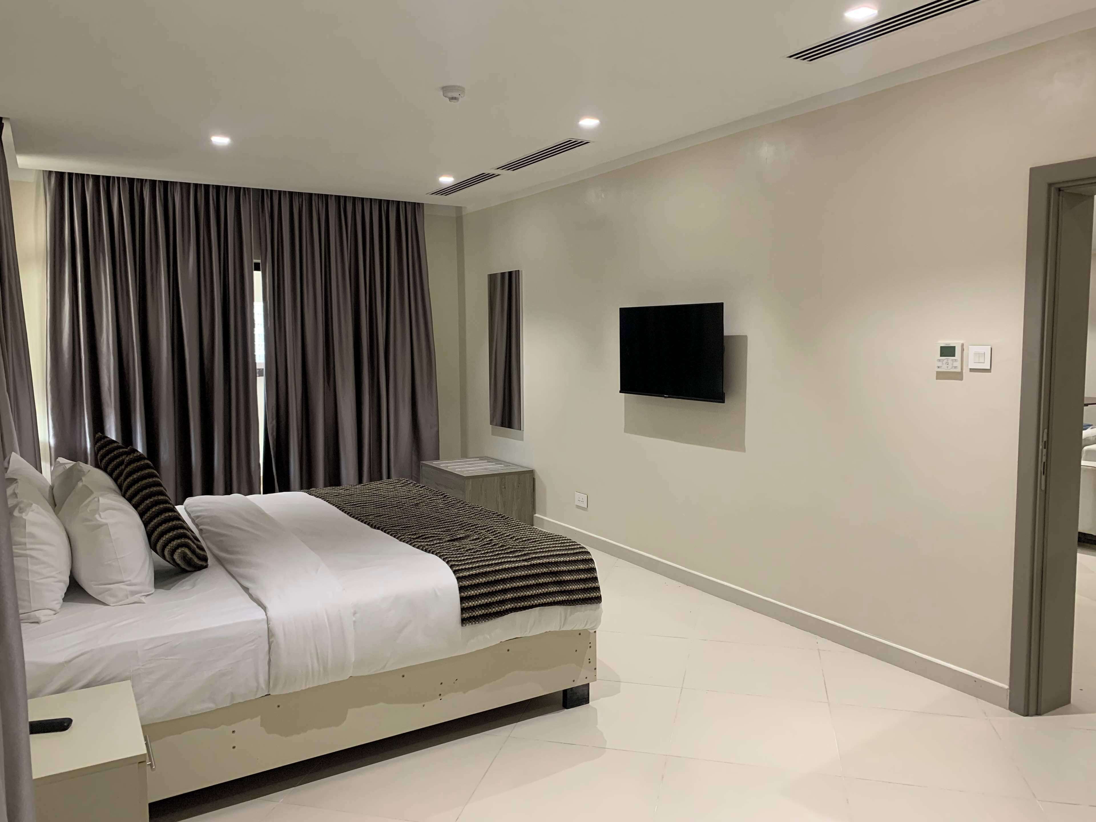 Una camera da letto moderna con un letto, tende, una TV a parete e un termostato.