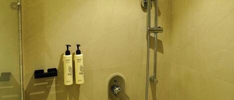 Doccia con soffione a mano, rubinetto a parete, porta in vetro e due flaconi di shampoo fissati alla parete.