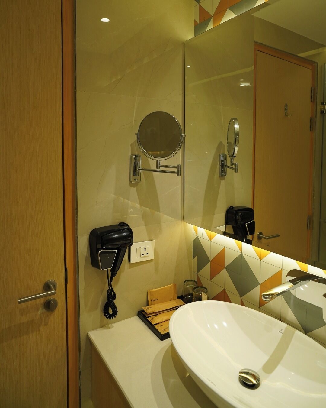 A bathroom with a large mirror, a hairdryer, a sink, and a towel rack.