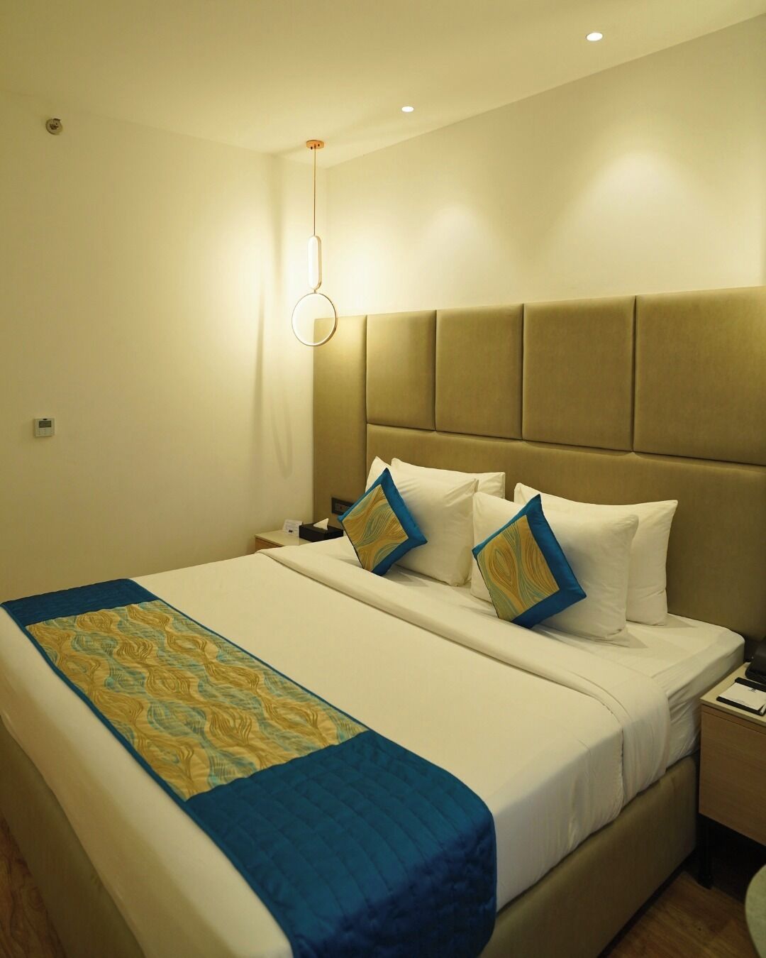 Una habitación de hotel con una cama, una mesita de noche y una lámpara fijada en la pared.