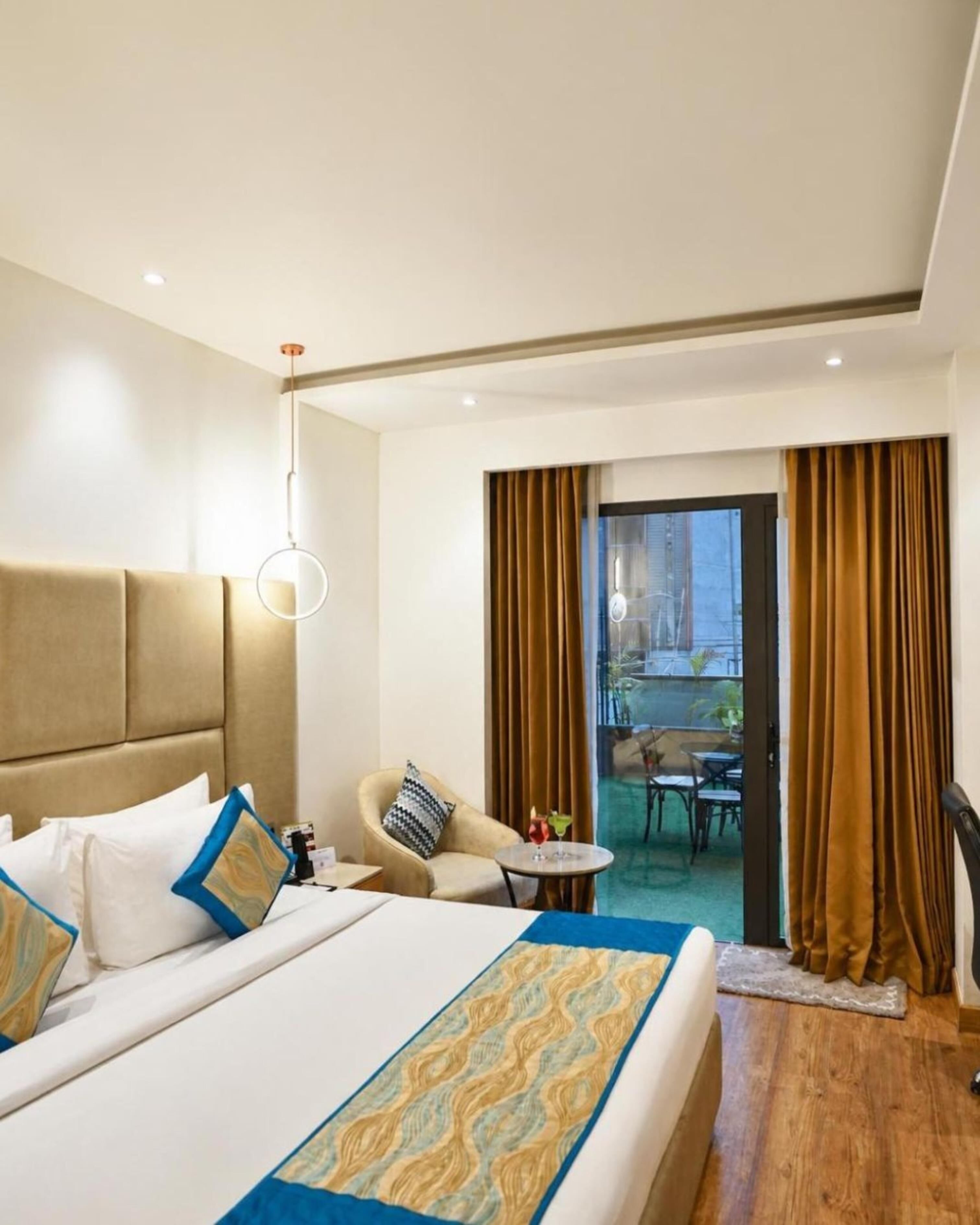 A hotel room with a bed, a chair, a small table, and a view of the outside.