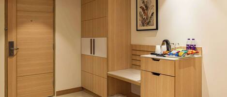 A modern room with wooden cabinetry, a white door, a small table with a kettle, and a trash bin.