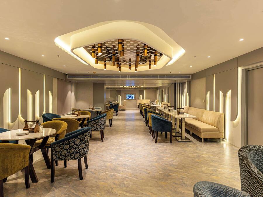 A modern hotel lobby with a central seating area, a long table, and a television screen.