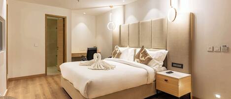 A modern hotel room with a large bed, bedside tables, and a wooden floor.