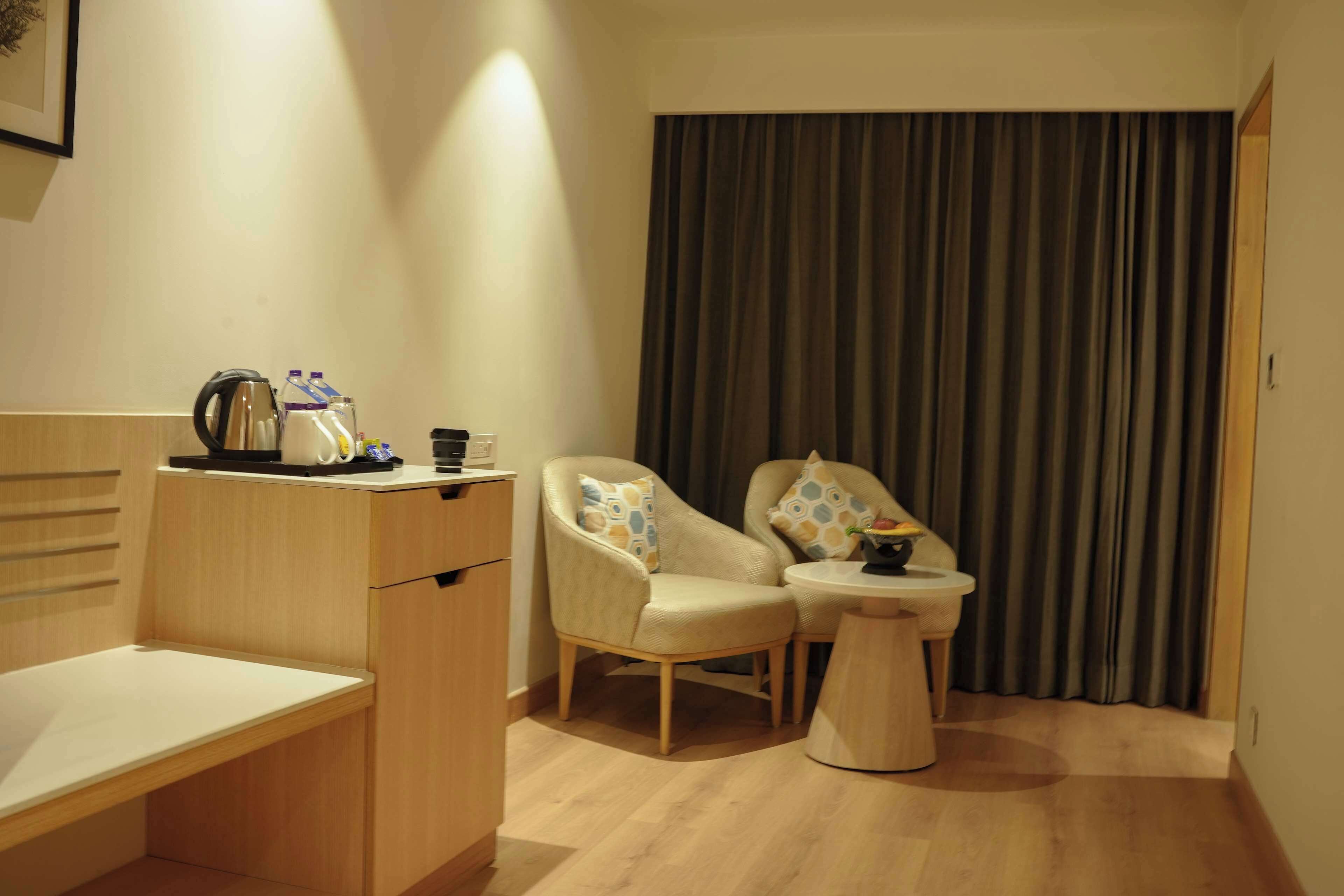 Una habitación de hotel con un escritorio de madera, dos sillones, una mesita y una cortina.