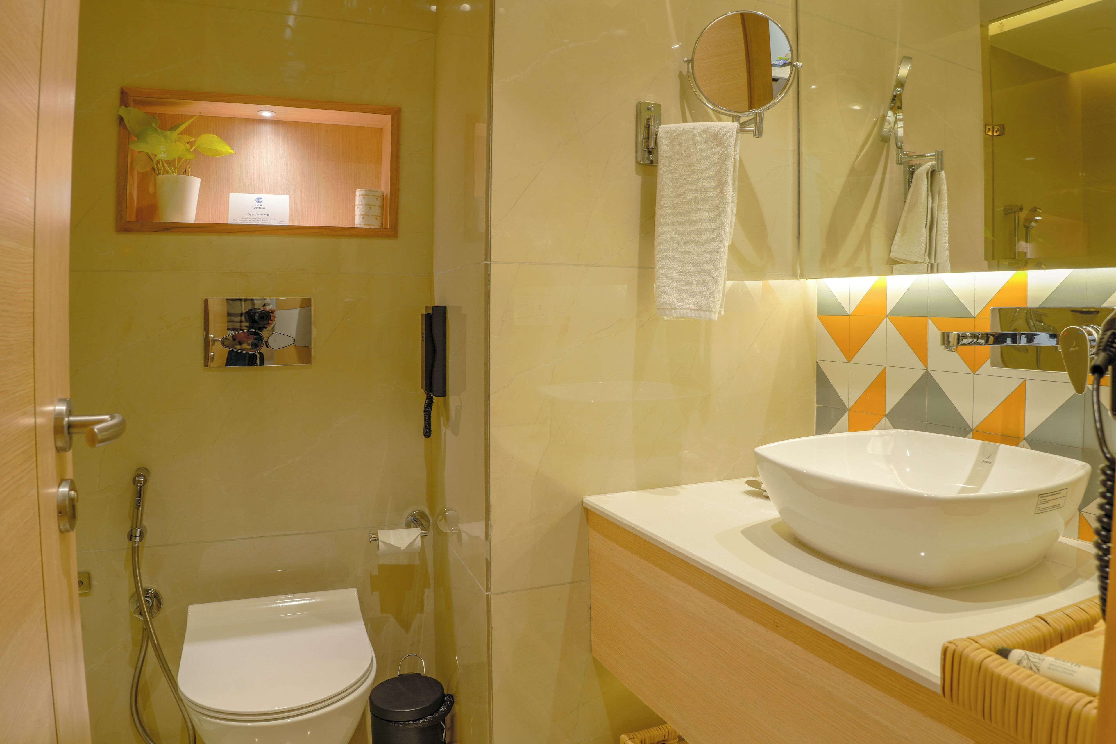 A bathroom with a toilet, a sink with a mirror, a shower, and a potted plant on the wall.