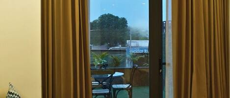 Ein Hotelzimmer mit Bett, Sessel, einem kleinen Tisch mit Getränken und Blick auf einen Außenbereich mit Tischen und Stühlen.