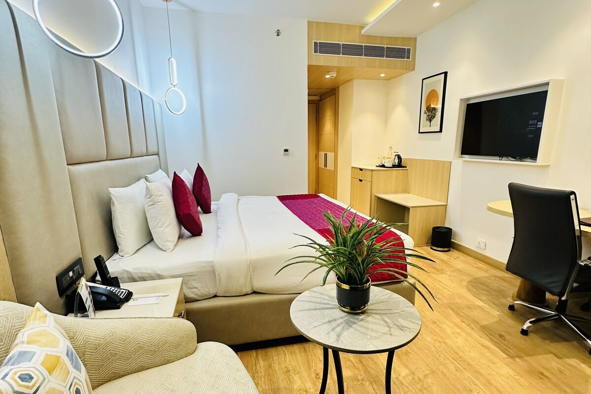 A modern hotel room with a bed, sofa, round table, and a TV.