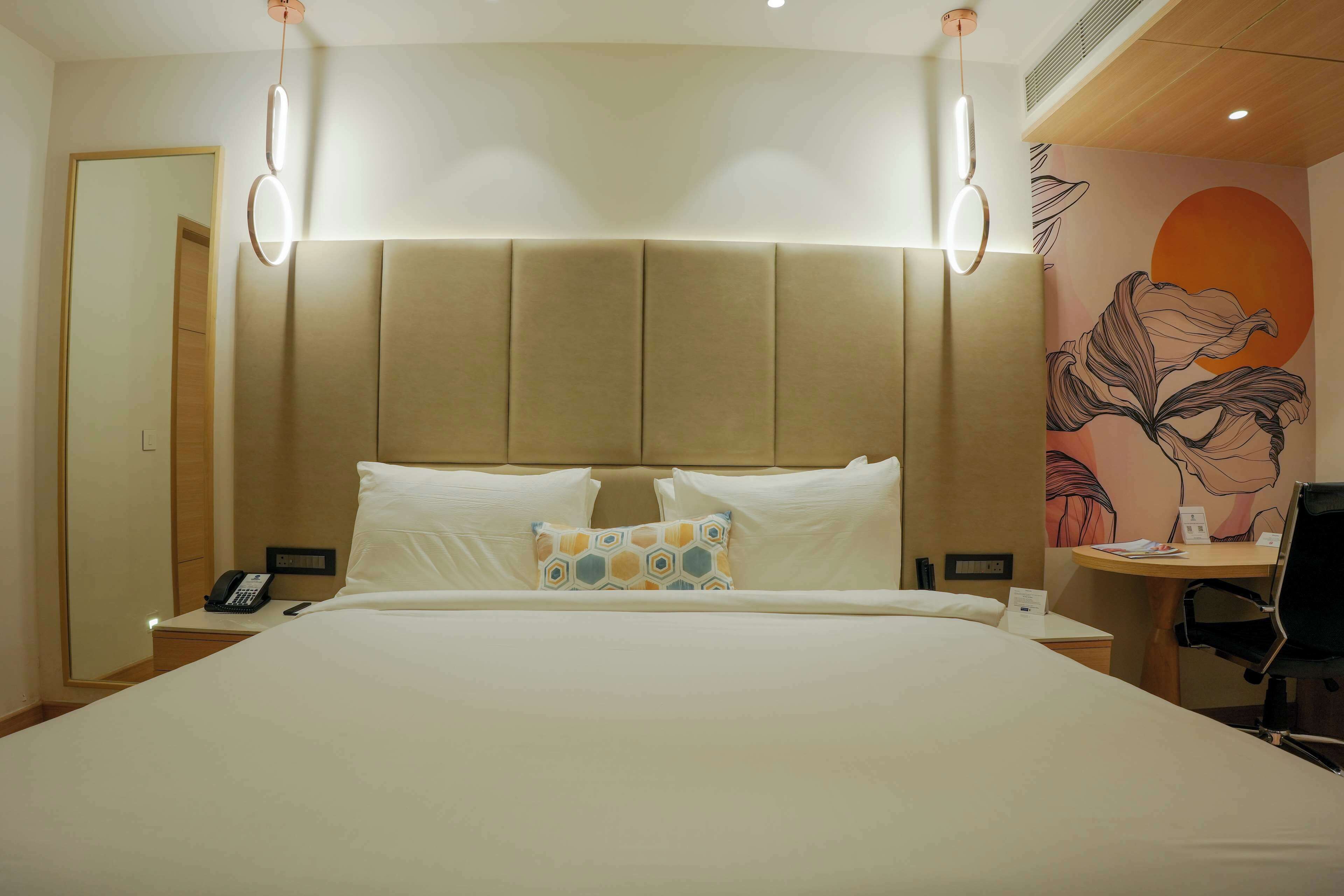 A hotel room with a large bed, a desk with a chair, a phone, and a wall with a floral mural.