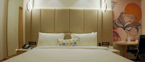 A hotel room with a large bed, a desk with a chair, a phone, and a wall with a floral mural.