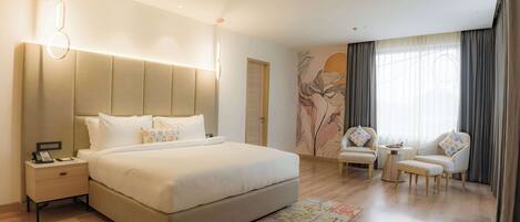 A modern hotel room with a large bed, bedside tables, a small table, two armchairs, and a decorative wall mural.