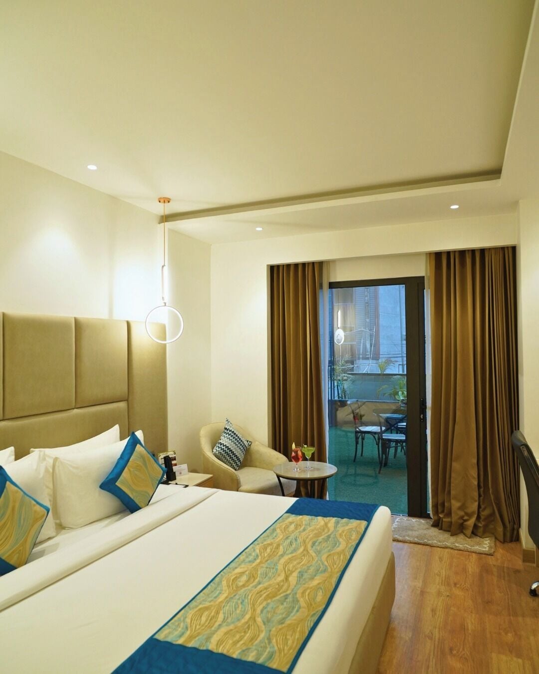A hotel room with a large bed, a chair, a small table, and a view of the outdoor area.