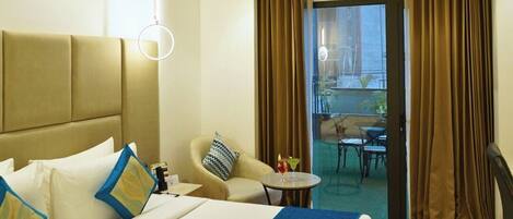 A hotel room with a large bed, a chair, a small table, and a view of the outdoor area.