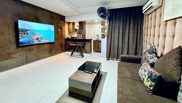 Ein modernes Wohnzimmer mit Flachbildfernseher, einer Couch, einem Couchtisch und einer Küchenzeile im Hintergrund.