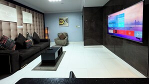 Ein modernes Wohnzimmer mit großem, an der Wand montierten Flachbildfernseher, gepolstertem Sofa, Couchtisch und Stehlampe.