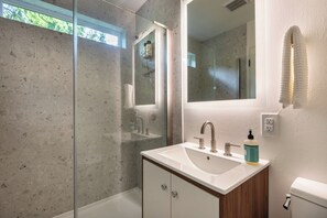 Ein modernes Badezimmer mit Duschkabine aus Glas, einem weißen Waschbecken mit Holzschrank und einem großen Spiegel.