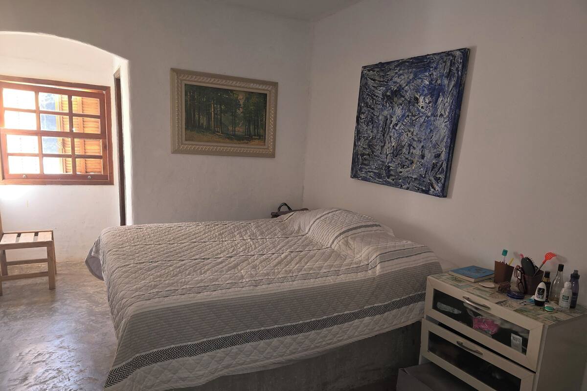 Un dormitorio con una cama, una silla, un tocador y un cuadro en la pared.