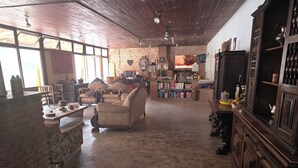 Un ampio soggiorno con parete in mattoni, soffitto in legno e camino. Sono presenti diverse zone relax, una libreria e un televisore.