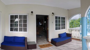 Une véranda abritée avec deux canapés en osier, un paillasson et une vue sur l’intérieur de la maison.