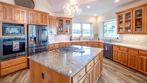 A modern kitchen with wooden cabinets, stainless steel appliances, a granite countertop, and a large island. - Whitehurst Lookout on the Sound (Beaufort)