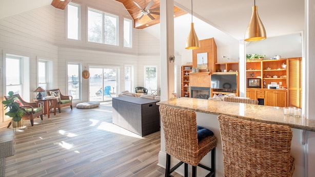 A spacious living area with a high ceiling, large windows, a kitchen with wooden cabinets, and a bar area with wicker chairs. - Whitehurst Lookout on the Sound (Beaufort)