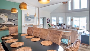 A dining area with a black table and woven placemats, a sofa with cushions, and a ceiling with pendant lights. - Whitehurst Lookout on the Sound (Beaufort)